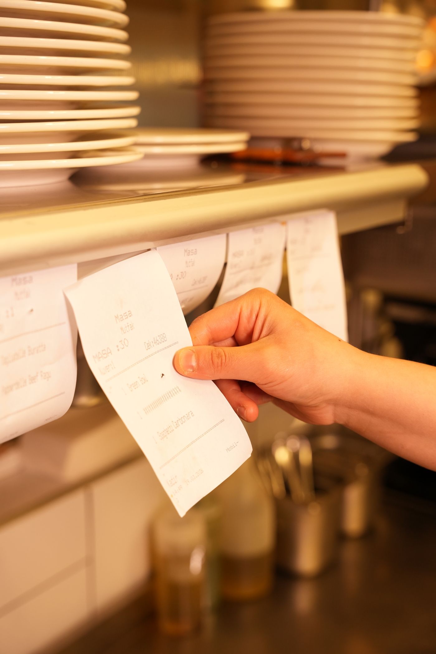 A hand pulling a paper order ticket from a kitchen rail